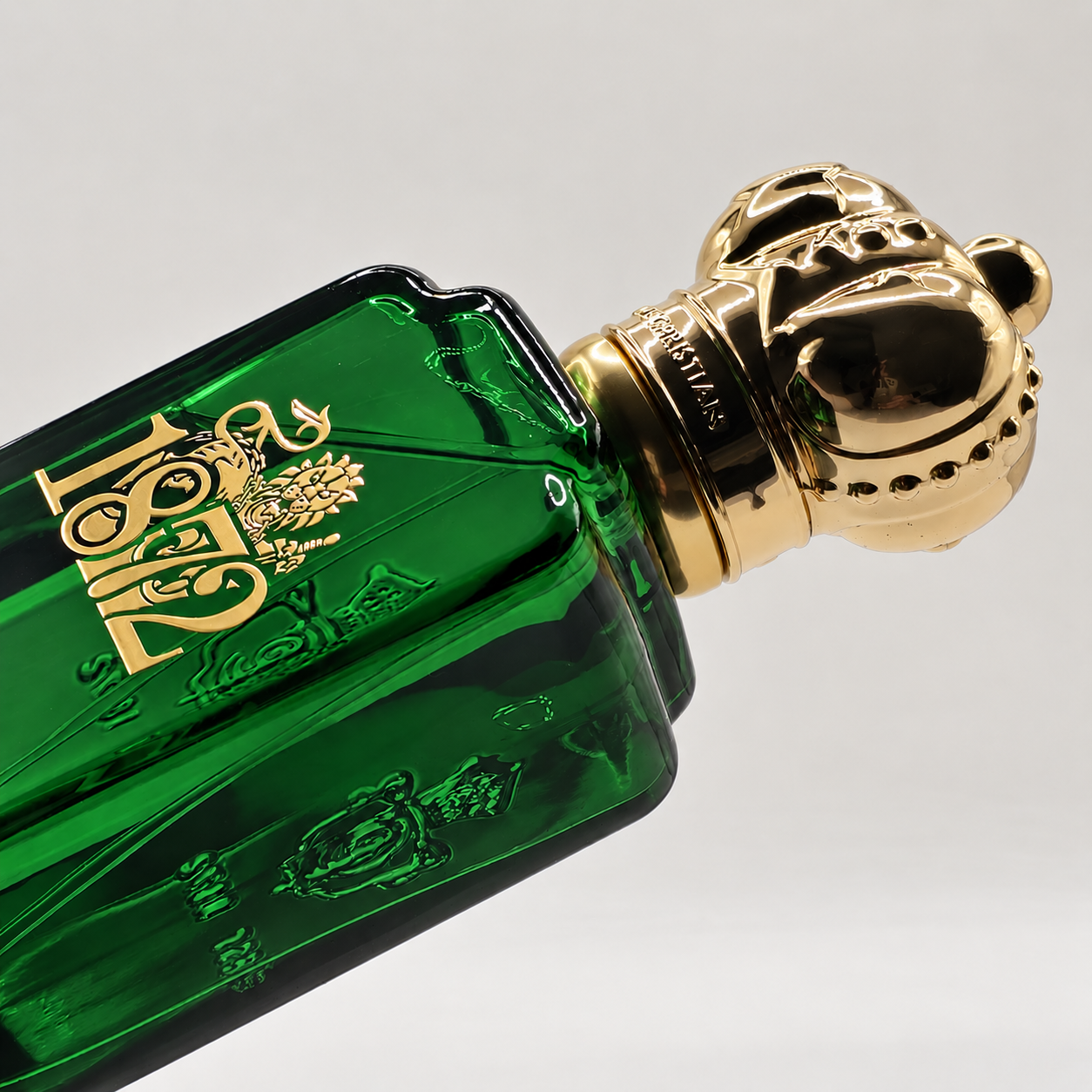 Image of Close-up of a Clive Christian 1872 perfume bottle in deep green glass with ornate gold detailing and a crown-shaped cap.